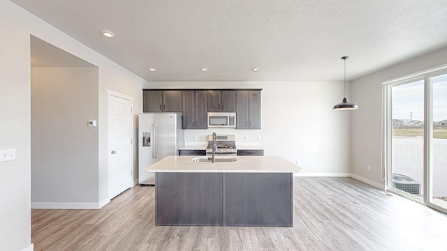 kitchen with a sink, light countertops, appliances with stainless steel finishes, an island with sink, and dark brown cabinets