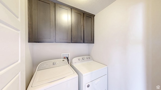 washroom with a textured ceiling, cabinet space, and washer and clothes dryer