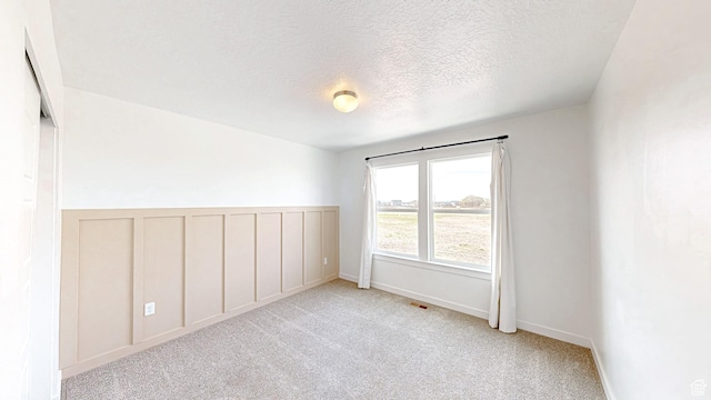 carpeted empty room with a textured ceiling, a decorative wall, and visible vents