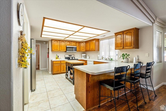 kitchen featuring brown cabinets, appliances with stainless steel finishes, light countertops, and a peninsula