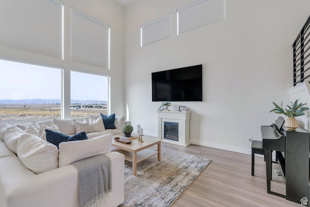 2888 E Carriage Hill Dr, Eagle Mountain, UT 84005 - living area with a glass covered fireplace, a towering ceiling, light wood-style floors, and baseboards