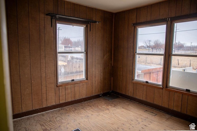 empty room with wood walls, light wood-style flooring, and baseboards