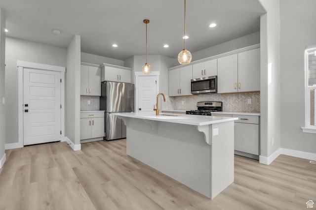 kitchen with light countertops, appliances with stainless steel finishes, a kitchen bar, and light wood finished floors