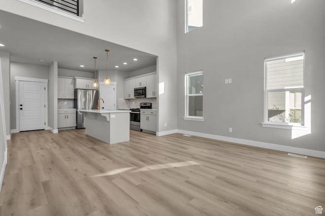 unfurnished living room featuring a towering ceiling, light wood-type flooring, baseboards, recessed lighting, and a sink