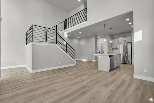 kitchen featuring light wood-type flooring, baseboards, light countertops, a center island with sink, and stainless steel appliances