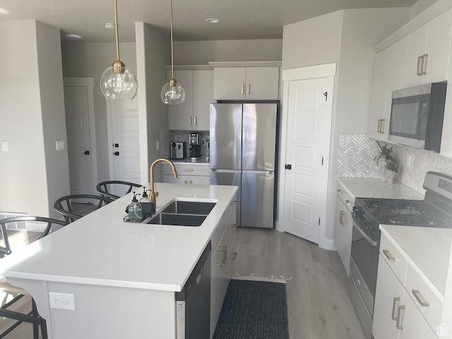 kitchen featuring a kitchen bar, a kitchen island with sink, a sink, stainless steel appliances, and light wood finished floors