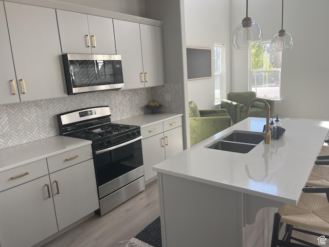 kitchen with a kitchen breakfast bar, light countertops, a sink, stainless steel appliances, and backsplash