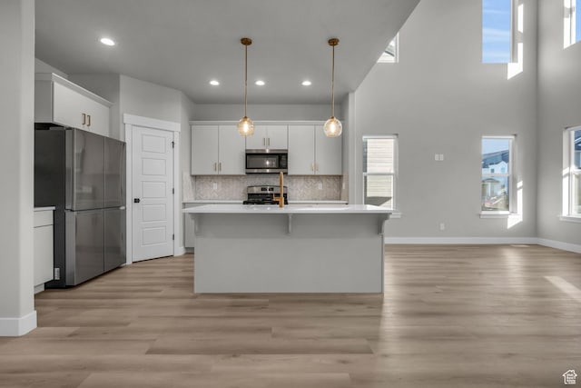 kitchen featuring white cabinets, light countertops, light wood-type flooring, appliances with stainless steel finishes, and decorative backsplash