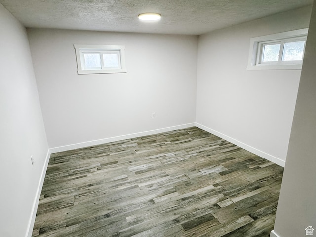spare room featuring a textured ceiling, wood finished floors, baseboards, and plenty of natural light