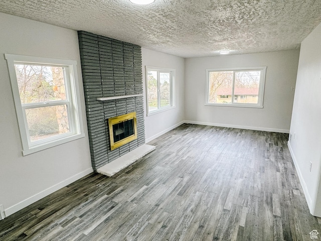 unfurnished living room with a textured ceiling, wood finished floors, a fireplace, and baseboards