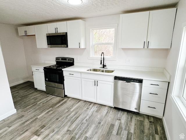 kitchen featuring light wood-style flooring, a textured ceiling, white cabinets, a sink, and stainless steel appliances