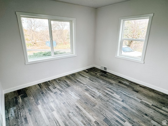spare room with plenty of natural light, visible vents, baseboards, and wood finished floors
