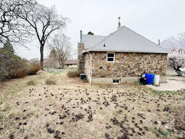 view of side of home featuring central air condition unit, stone siding, and a chimney