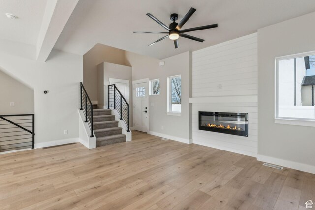 unfurnished living room featuring ceiling fan, a fireplace, light wood-type flooring, stairway, and baseboards