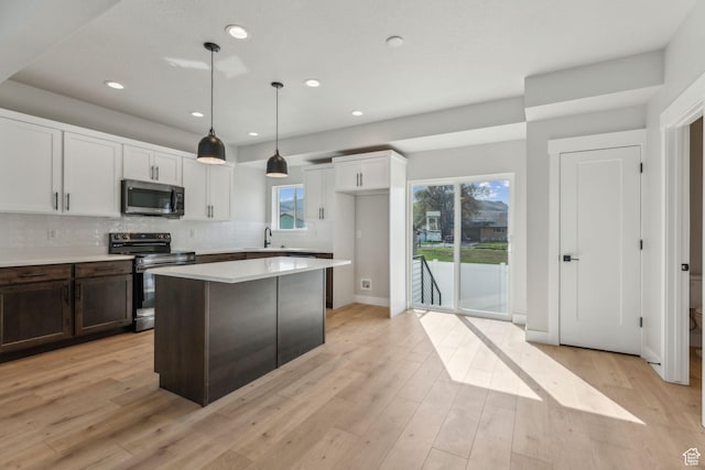 kitchen with a wealth of natural light, appliances with stainless steel finishes, a sink, light wood finished floors, and decorative backsplash