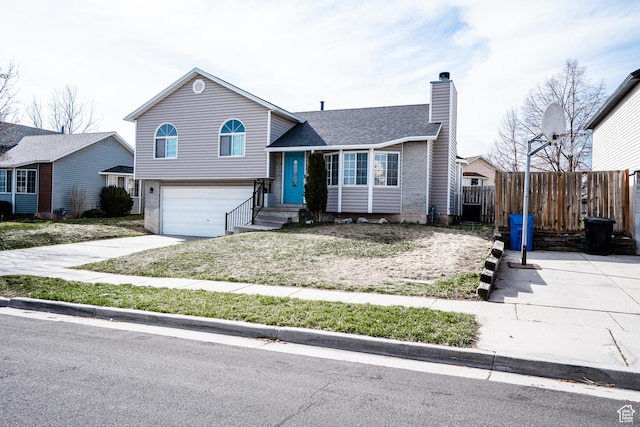 tri-level home with a garage, a chimney, fence, and concrete driveway