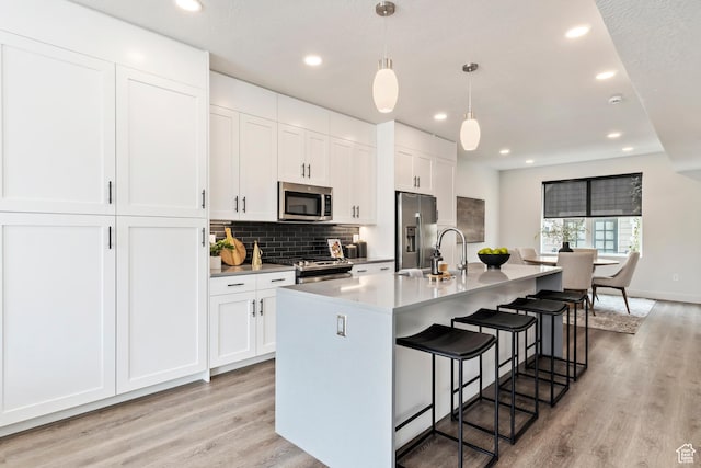 kitchen with white cabinets, an island with sink, a kitchen bar, light wood finished floors, and stainless steel appliances
