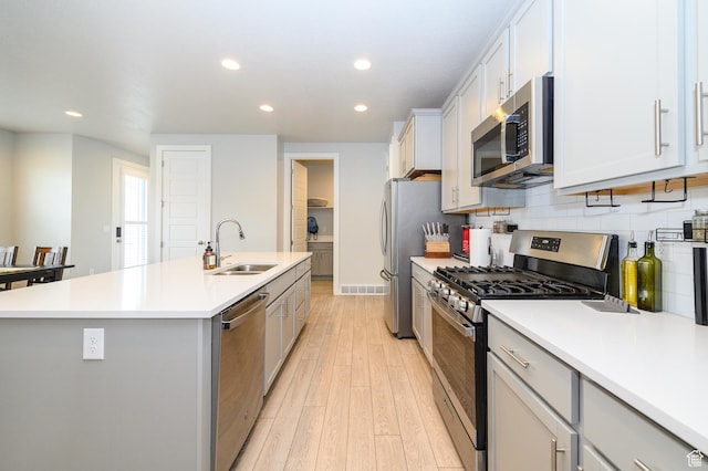 11531 S Bingham Rim Rd, South Jordan, UT 84009 - kitchen with light wood-style floors, a sink, stainless steel appliances, a center island with sink, and decorative backsplash