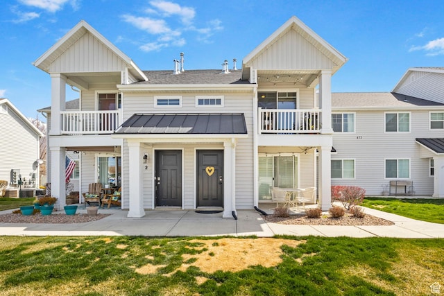 view of property featuring a standing seam roof, a patio, metal roof, a front yard, and a balcony