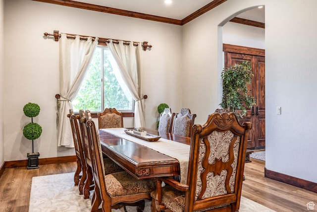 dining space featuring arched walkways, baseboards, ornamental molding, and light wood-type flooring