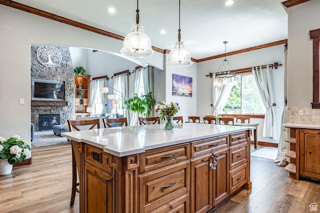 kitchen with a fireplace, brown cabinets, crown molding, light wood-style flooring, and a breakfast bar area