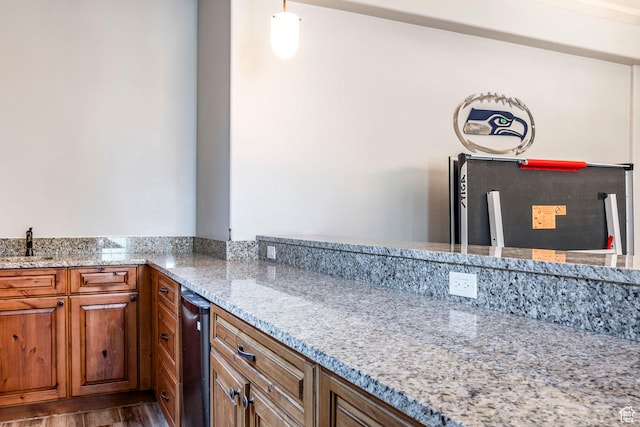 kitchen with brown cabinetry, wood finished floors, a sink, and light stone counters