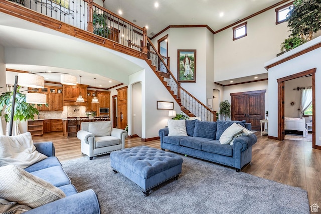 living room with baseboards, arched walkways, ornamental molding, stairs, and light wood-style flooring