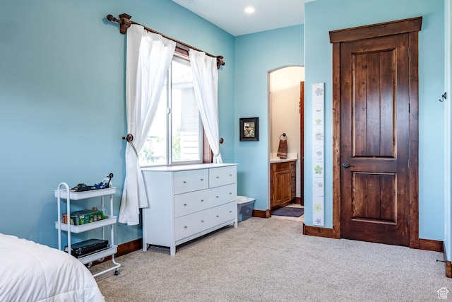 carpeted bedroom with ensuite bathroom, baseboards, and arched walkways