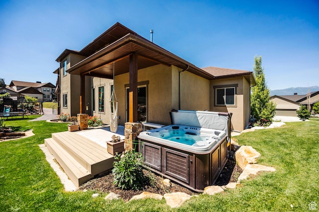 rear view of property with a yard, a deck, stucco siding, and a hot tub