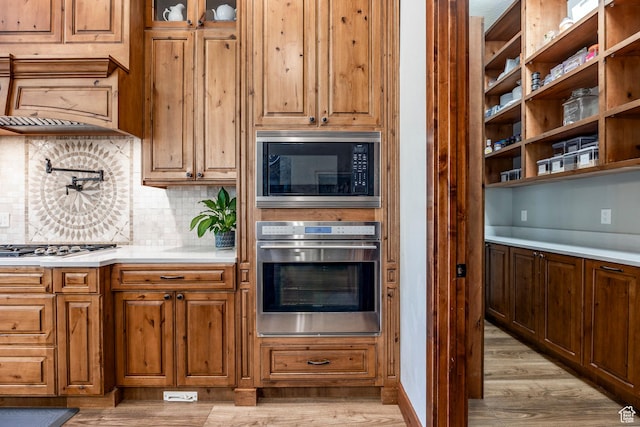 kitchen featuring brown cabinetry, light wood-type flooring, appliances with stainless steel finishes, light countertops, and decorative backsplash