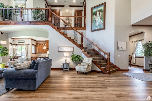 living room featuring crown molding, arched walkways, stairway, a high ceiling, and wood finished floors