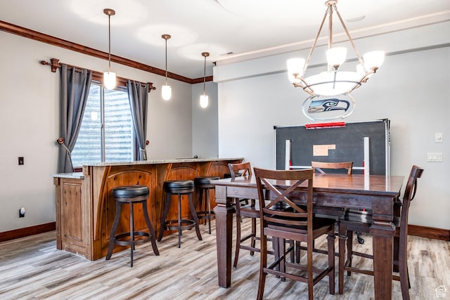 dining space with ornamental molding, baseboards, light wood finished floors, and a bar