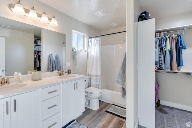 full bath with a sink, a spacious closet, toilet, double vanity, and wood finished floors