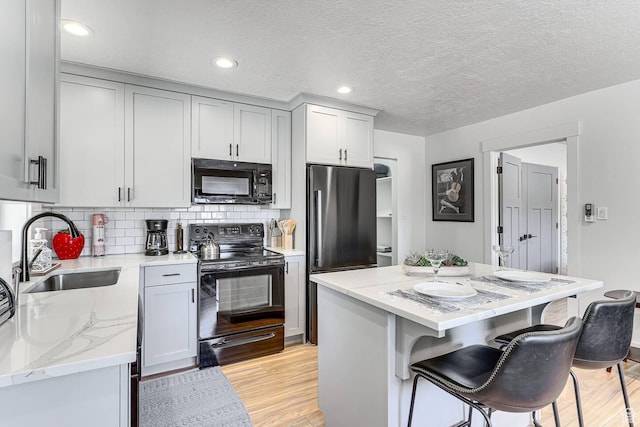 kitchen with light stone counters, light wood-style flooring, black appliances, a kitchen bar, and a sink