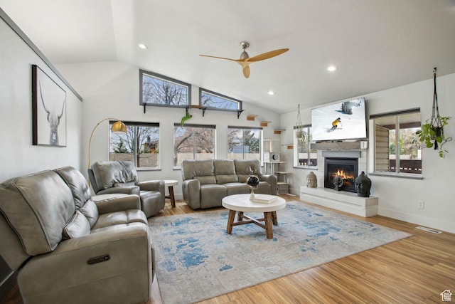 living room featuring a warm lit fireplace, wood finished floors, ceiling fan, and vaulted ceiling
