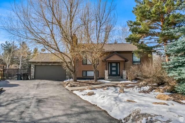 bi-level home featuring an attached garage, fence, and aphalt driveway