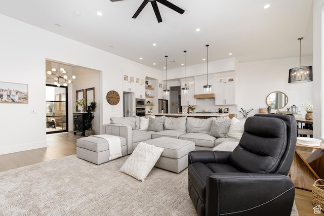 living area with baseboards, recessed lighting, light wood-style floors, and ceiling fan with notable chandelier