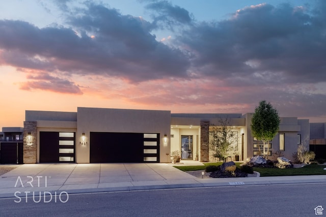 view of front of house with stone siding, a garage, stucco siding, and concrete driveway