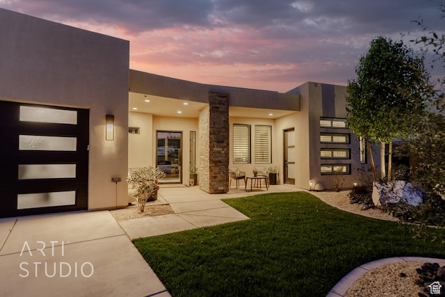 exterior entry at dusk featuring a yard, stucco siding, and a patio area