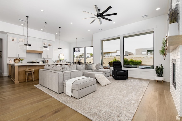 living area with recessed lighting, a fireplace, light wood-style flooring, and a ceiling fan