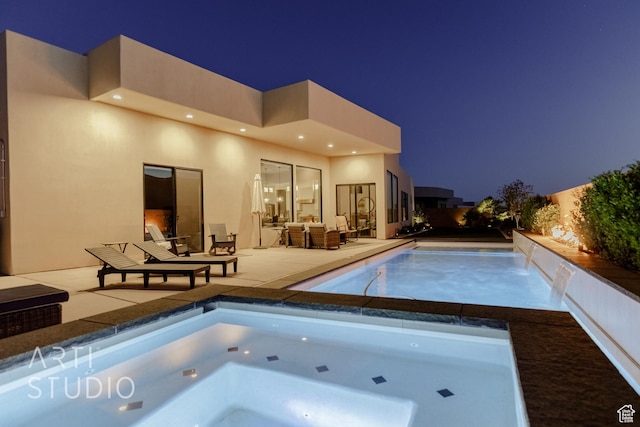 pool at night with a patio area and an in ground hot tub