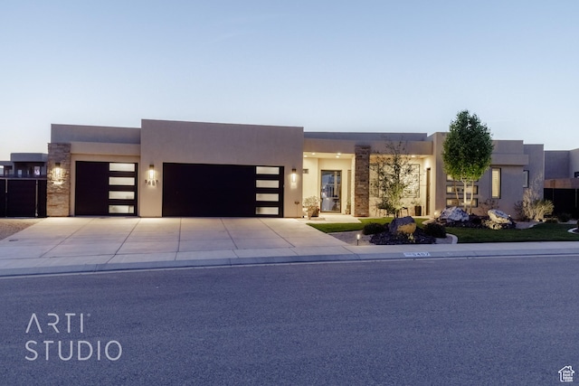 view of front of house featuring a garage, driveway, stone siding, and stucco siding