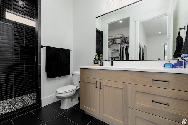 full bathroom featuring vanity, tile patterned flooring, toilet, a walk in closet, and a tile shower
