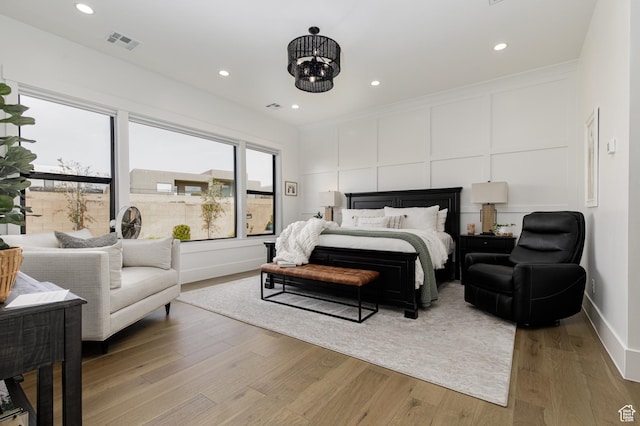 bedroom with a decorative wall, visible vents, recessed lighting, a chandelier, and light wood finished floors