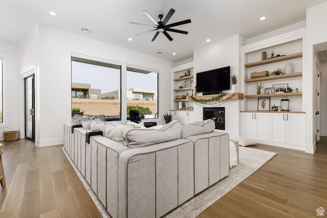 living room with built in features, ceiling fan, a fireplace, light wood finished floors, and recessed lighting