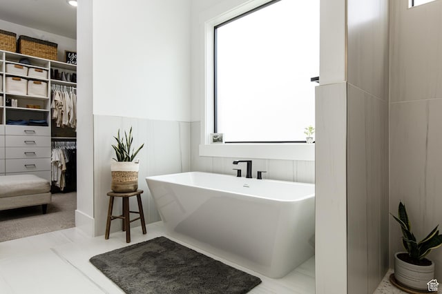 bathroom featuring a spacious closet, plenty of natural light, and a soaking tub