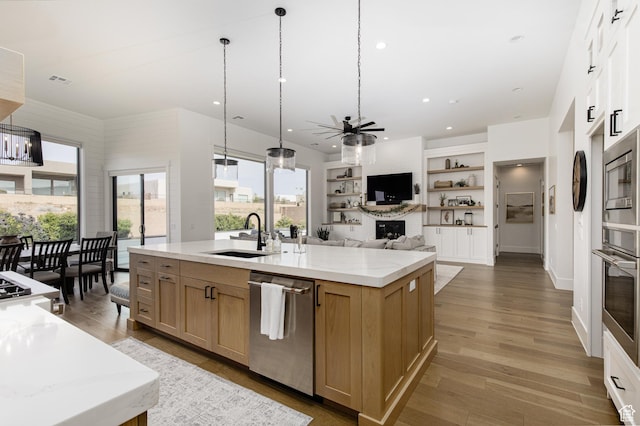 kitchen featuring appliances with stainless steel finishes, a kitchen island with sink, ceiling fan, light wood finished floors, and a sink