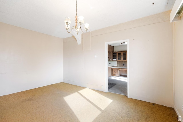 spare room featuring light colored carpet and a notable chandelier