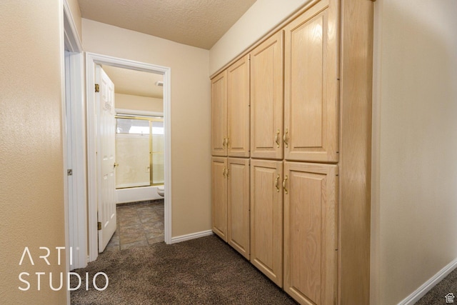 hall featuring dark carpet, baseboards, and a textured ceiling