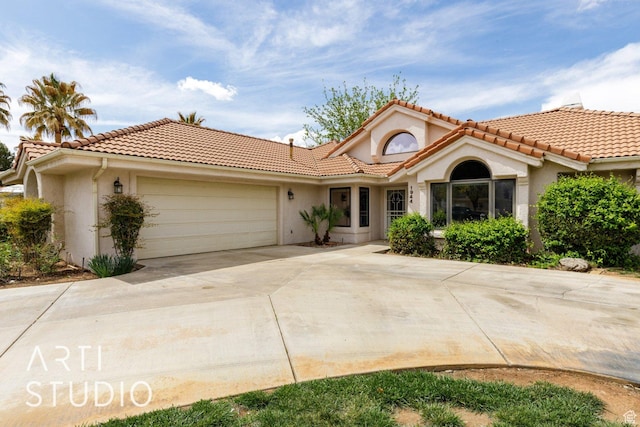 mediterranean / spanish-style home featuring an attached garage, a tiled roof, driveway, and stucco siding